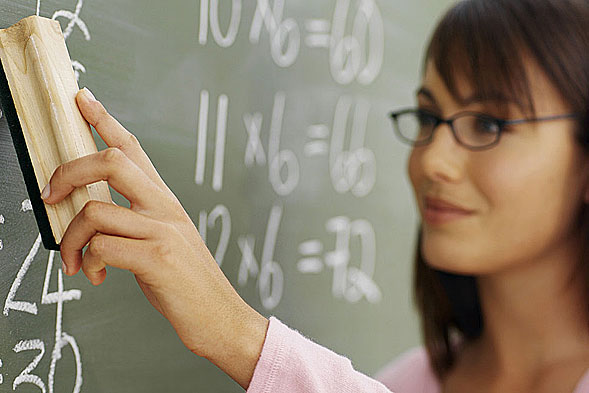 Healthy attractive female teacher wearing glasses facing left wiping a board